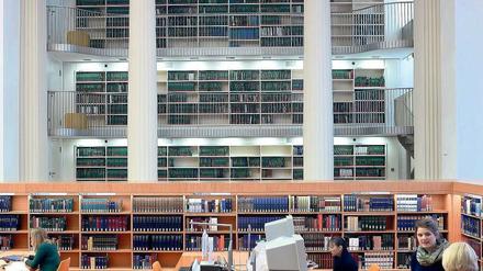 Frauen stehen in einer Bibliothek oder sitzen dort am Computer.