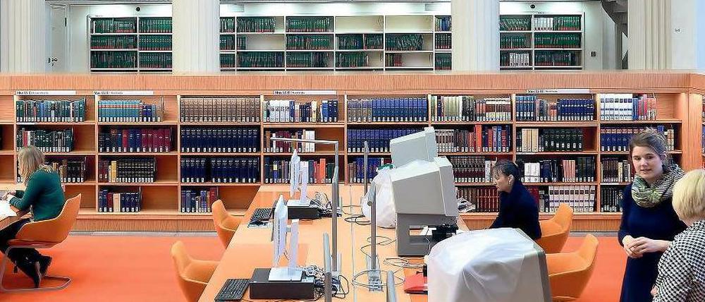 Frauen stehen in einer Bibliothek oder sitzen dort am Computer.