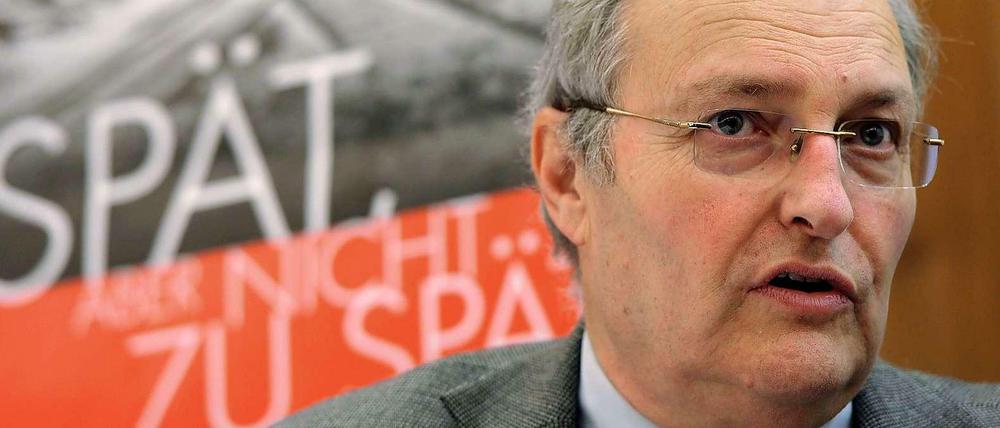 Efraim Zuroff, Direktor des Wiesenthal-Zentrums in Israel, vor dem Plakat der Kampagne. Auf dem Plakat steht: "Spät, aber nicht zu spät", im Hintergrund das Tor des Vernichtungslagers Auschwitz.