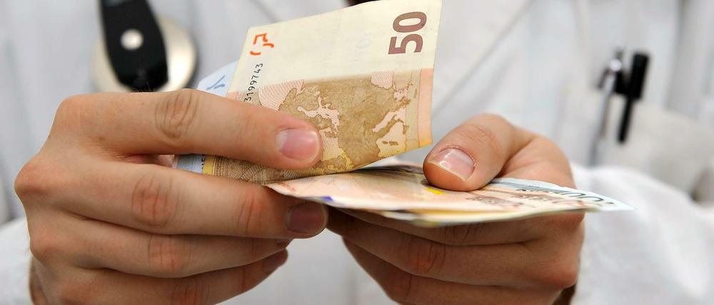 Ein Arzt hält Geldscheine in der Hand.
