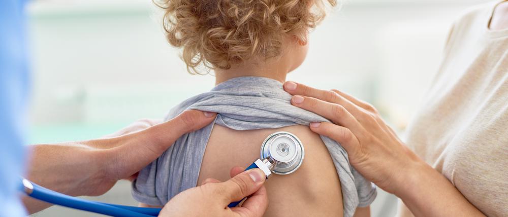 Unrecognizable male pediatrician examining curly little patient with help of stethoscope, blurred background