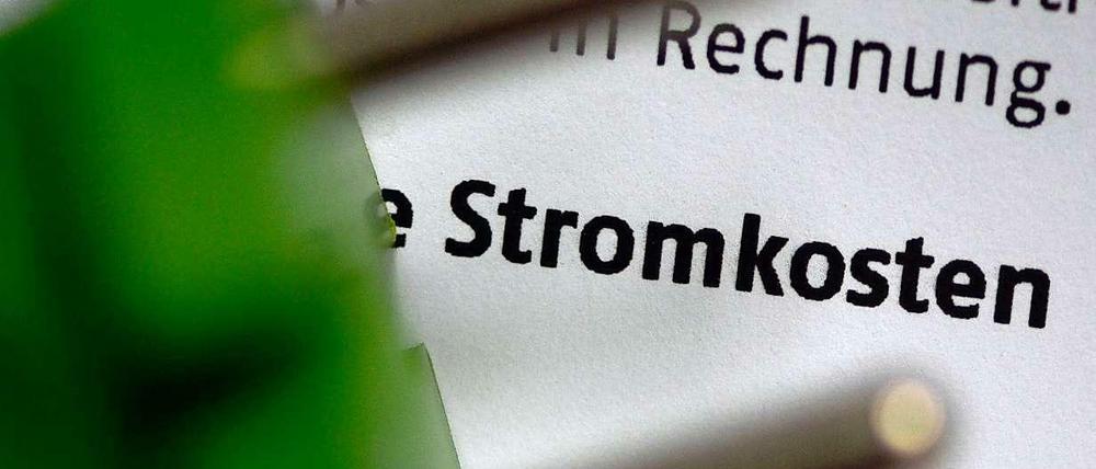 Ein grüner Stecker vor einem Papier, auf dem das Wort "Stromkosten" zu lesen ist.