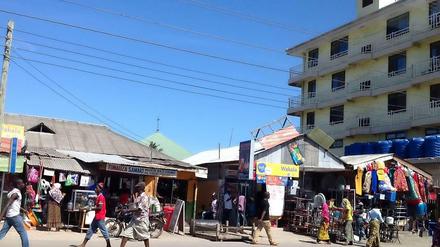 Afrikanische Einkaufsmeile. In Wellblechhütten am Straßenrand gibt es unter anderem bunte Stoffe, Obst, Gemüse und Wasser in Plastikbeuteln.