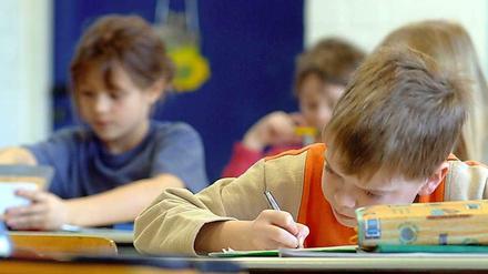 Grundschüler sitzen in einer Klasse an ihren Tischen und schreiben.