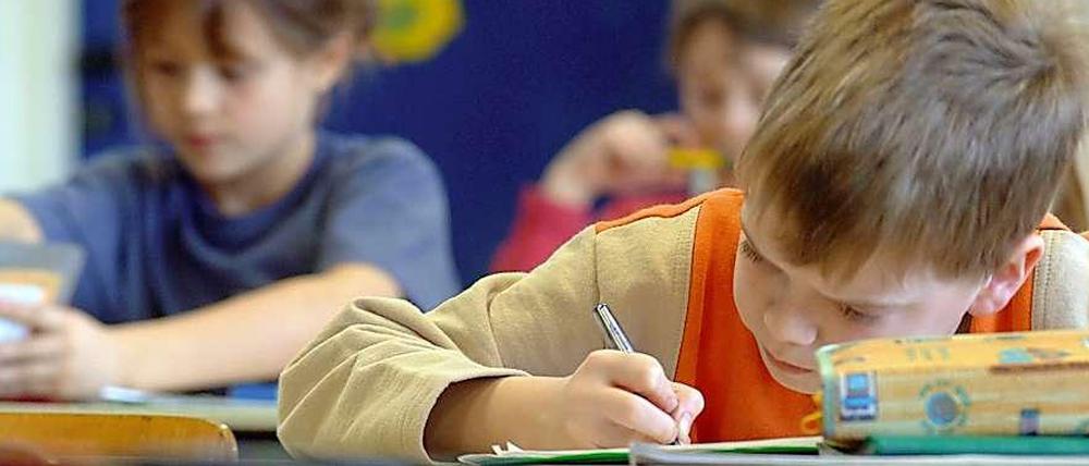 Grundschüler sitzen in einer Klasse an ihren Tischen und schreiben.