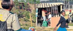 In einem Township in Johannesburg steht eine Gartenarbeiterin an einem Weg, auf dem ein Mädchen in Schuluniform vorbeigeht.