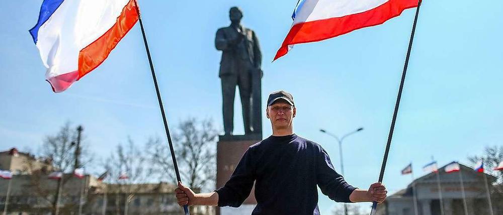 Ein Mann steht mit Fahnen der autonomen Republik Krim vor dem Lenin-Denkmal in Simferopol