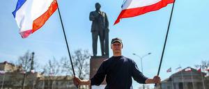 Ein Mann steht mit Fahnen der autonomen Republik Krim vor dem Lenin-Denkmal in Simferopol