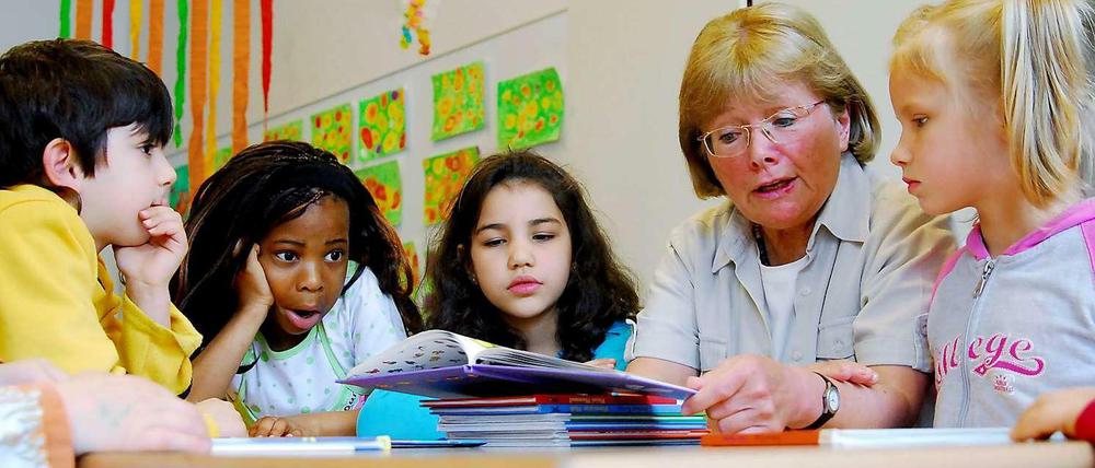 Eine Lesepatin liest vier Grundschulkindern aus einem Bilderbuch vor.