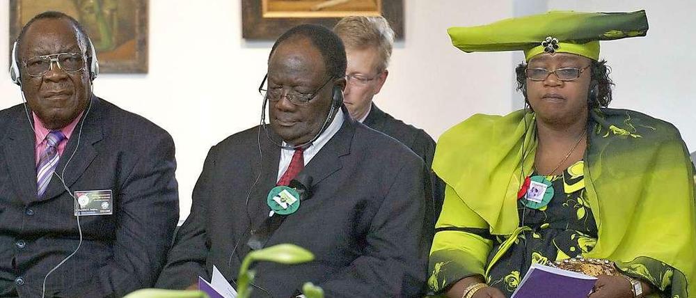 Opfer-Vertreter aus Namibia sitzen bei einer Berliner Trauerfeier im Jahr 2011 vor einem Schaukasten mit Schädeln.