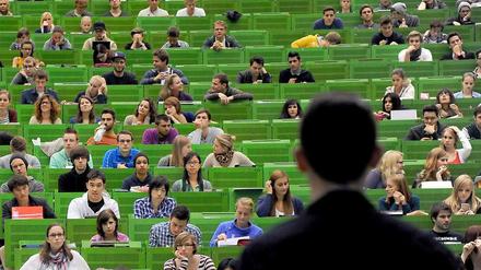 Ein junger Professor steht vor Studierenden im Hörsaal.