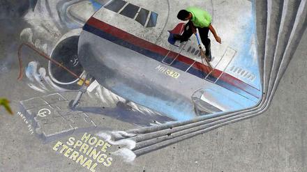 Ein Straßenarbeiter fegt ein Bild von Flug MH 370 in Manila. 