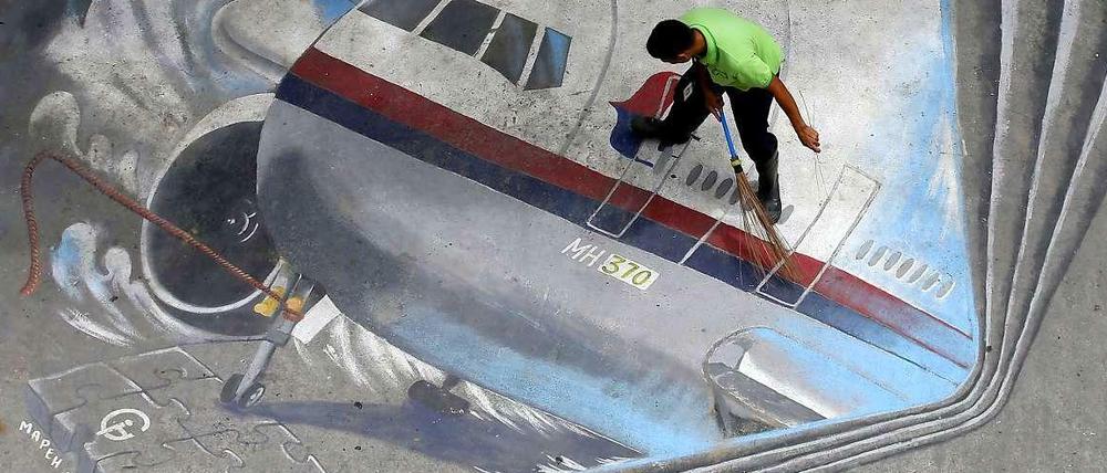 Ein Straßenarbeiter fegt ein Bild von Flug MH 370 in Manila.