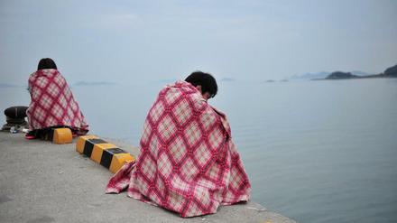 Überlebende des Fährunglücks sitzen nach ihrer Rettung auf einer Hafenmole und schauen auf das Meer hinaus. 