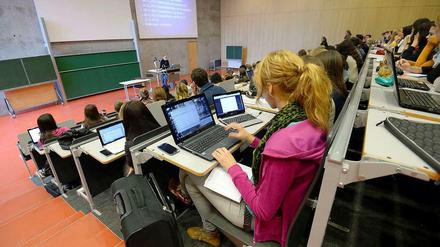 Studierende sitzen in einem Hörsaal, ein Professor steht an einem Stehpult und zeigt eine Powerpointpräsentation.
