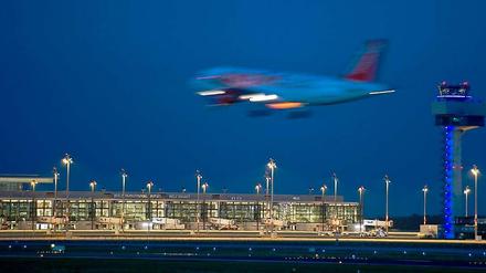 Ein Passagierflugzeug landet neben dem hell erleuchteten Berlin Brandenburg Airport Willy Brandt (BER) in Schönefeld (Brandenburg).