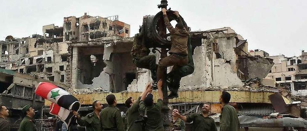 In der zerstörten Stadt Homs hissen Soldaten die syrische Fahne, nachdem die Rebellen abgezogen sind. 