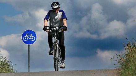 Radfahrer auf Radweg vor blauem Radwegschild.