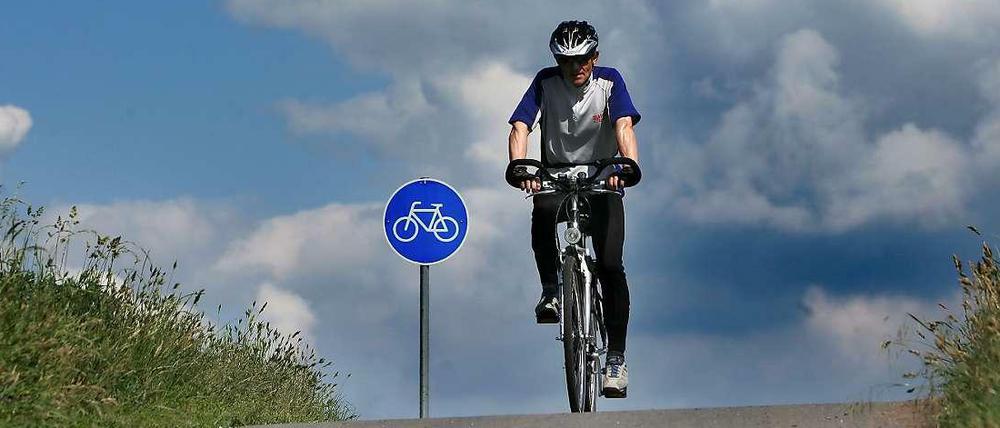 Radfahrer auf Radweg vor blauem Radwegschild.