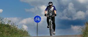 Radfahrer auf Radweg vor blauem Radwegschild.
