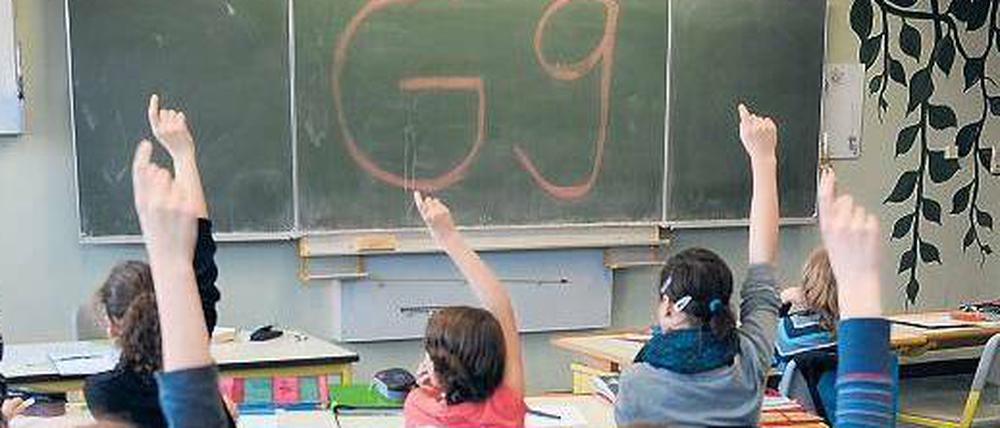 In einer Klasse steht der Schriftzug G9 an der Tafel, Schüler melden sich.
