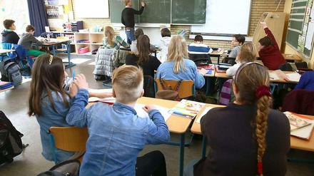 Ein Lehrer steht mit dem Rücken zur Klasse und schreibt Matheaufgaben an die Tafel.