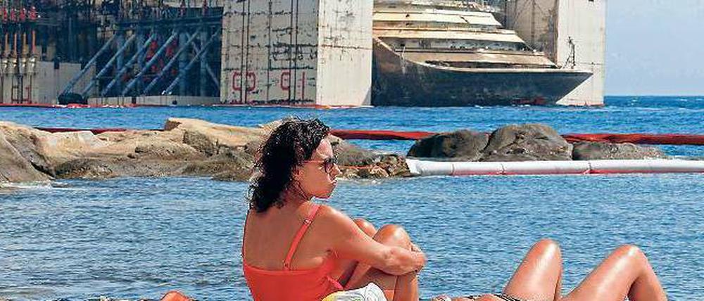 Hoch aufgerichtet präsentiert sich die Costa Concordia, während Strandbesucher den Tag genießen.
