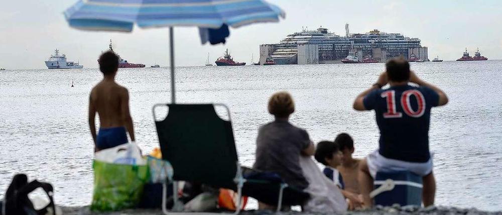 Vom Strand aus beobachten Urlauber, wie die Costa Concordia in Genua ankommt.