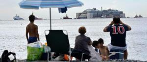 Vom Strand aus beobachten Urlauber, wie die Costa Concordia in Genua ankommt.