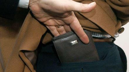 Die Hand eines Taschendiebes zieht seinem Opfer unbemerkt die Geldbörse aus der Gesäßtasche.
