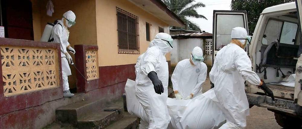 Ein Ebola-Opfer wird aus einem Haus in Liberia getragen. Ein Mitarbeiter des Gesundheitsdienstes desinfiziert das Haus, um eine Ansteckung seiner Bewohner weniger wahrscheinlich zu machen.