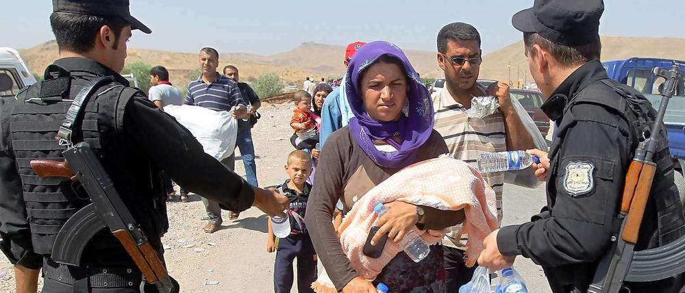 Bewaffnete Kräfte der kurdischen Peschmerga reichen jesidischen Flüchtlingen im Nordirak Wasserflaschen.
