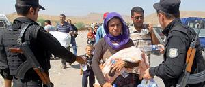 Bewaffnete Kräfte der kurdischen Peschmerga reichen jesidischen Flüchtlingen im Nordirak Wasserflaschen. 