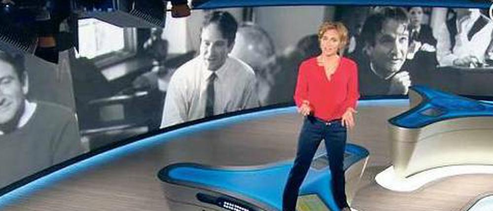 Große Geste. Caren Miosga steigt auf den Moderatorentisch und erinnert an eine besondere Filmszene mit Robin Williams.