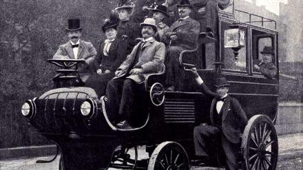 Auf einem kutschenähnlichen Fahrzeug sitzen Männer und Frauen auf dem Führerstand. Es handelt sich um einen Elektrobus mit Akkubetrieb, der 1899 von der Firma Kühlstein in Berlin gebaut wurde.