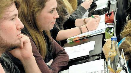 Junge Studierende sitzen im Hörsaal, vor sich Laptops und Schreibhefte.