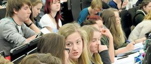 Junge Studierende sitzen im Hörsaal, vor sich Laptops und Schreibhefte.
