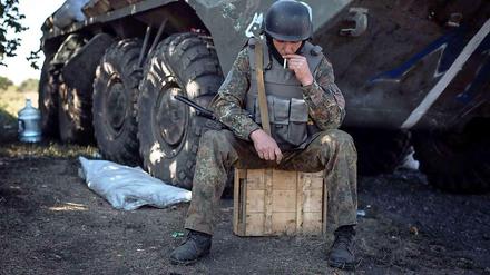 Soldat vor Panzer auf Kiste mit Zigarette, schaut nach unten
