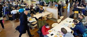 Studierende sitzen in einer Mensa und essen, ein Professor geht vorbei.