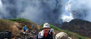 Wanderer steigen ab, während hinter ihnen der Vulkan Ontake explodiert.