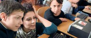 Kinder und Jugendliche und eine Lehrerin sitzen vor einer Reihe von Computern.