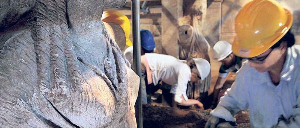 Ein Bild von der Ausgrabungsstätte, im Hintergrund arbeiten Archäologen.