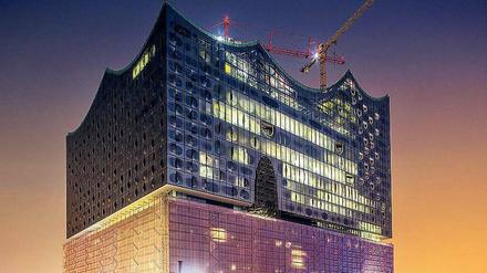Lichter der Großbaustelle. Die Elbphilharmonie, die auf einem Kai der Hafencity in den Fluss ragt, in abendlicher Beleuchtung. 