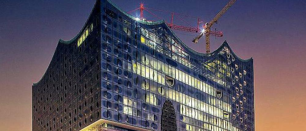 Lichter der Großbaustelle. Die Elbphilharmonie, die auf einem Kai der Hafencity in den Fluss ragt, in abendlicher Beleuchtung.