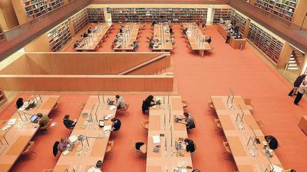 Im Lesesaal einer wissenschaftlichen Bibliothek sitzen Menschen an Tischen und lesen oder schreiben an Computern.