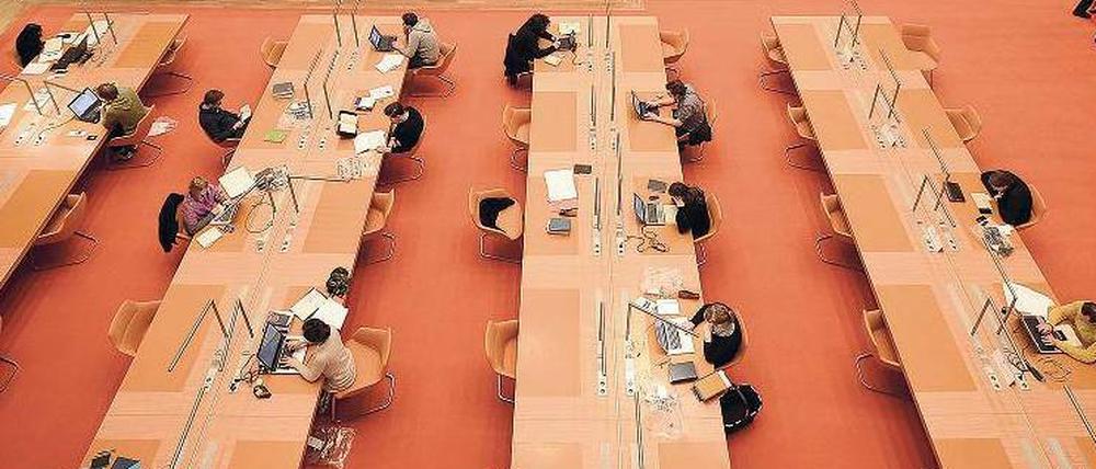 Im Lesesaal einer wissenschaftlichen Bibliothek sitzen Menschen an Tischen und lesen oder schreiben an Computern.