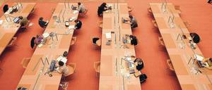Im Lesesaal einer wissenschaftlichen Bibliothek sitzen Menschen an Tischen und lesen oder schreiben an Computern.