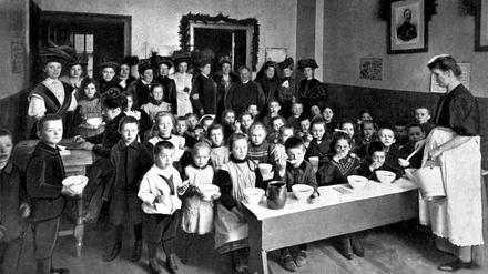 Eine Schar Kinder sitzt vor Suppenschüsseln in der Kreuzberger Kindervolksküche, von denen der jüdische Kaufmann Herrmann Abraham etwa ein Dutzend mit Spendengeldern betreibt.