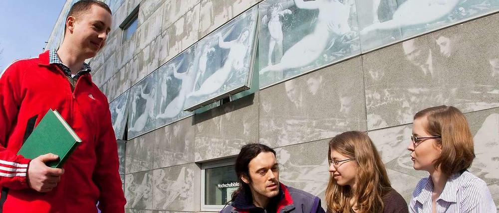 Studierende sitzen vor ihrer Hochschule.