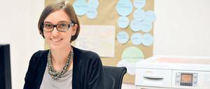 Eine junge Frau sitzt am Computer, im Hintergrund steht eine Waschmaschine.